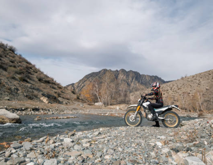 Female motorcyclist seating on Offroad enduro motorcycle in beautiful mountains near the river